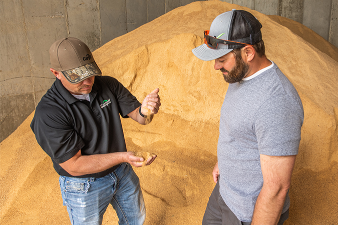 A cargill employee holding grain, with a farmer, next to a pile of grain